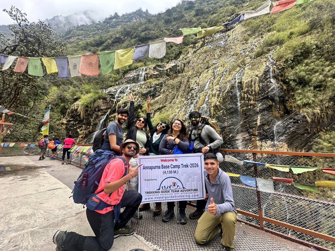 Annapurna Base Camp Trek 2026 group photo at waterfall with prayer flags Nepal