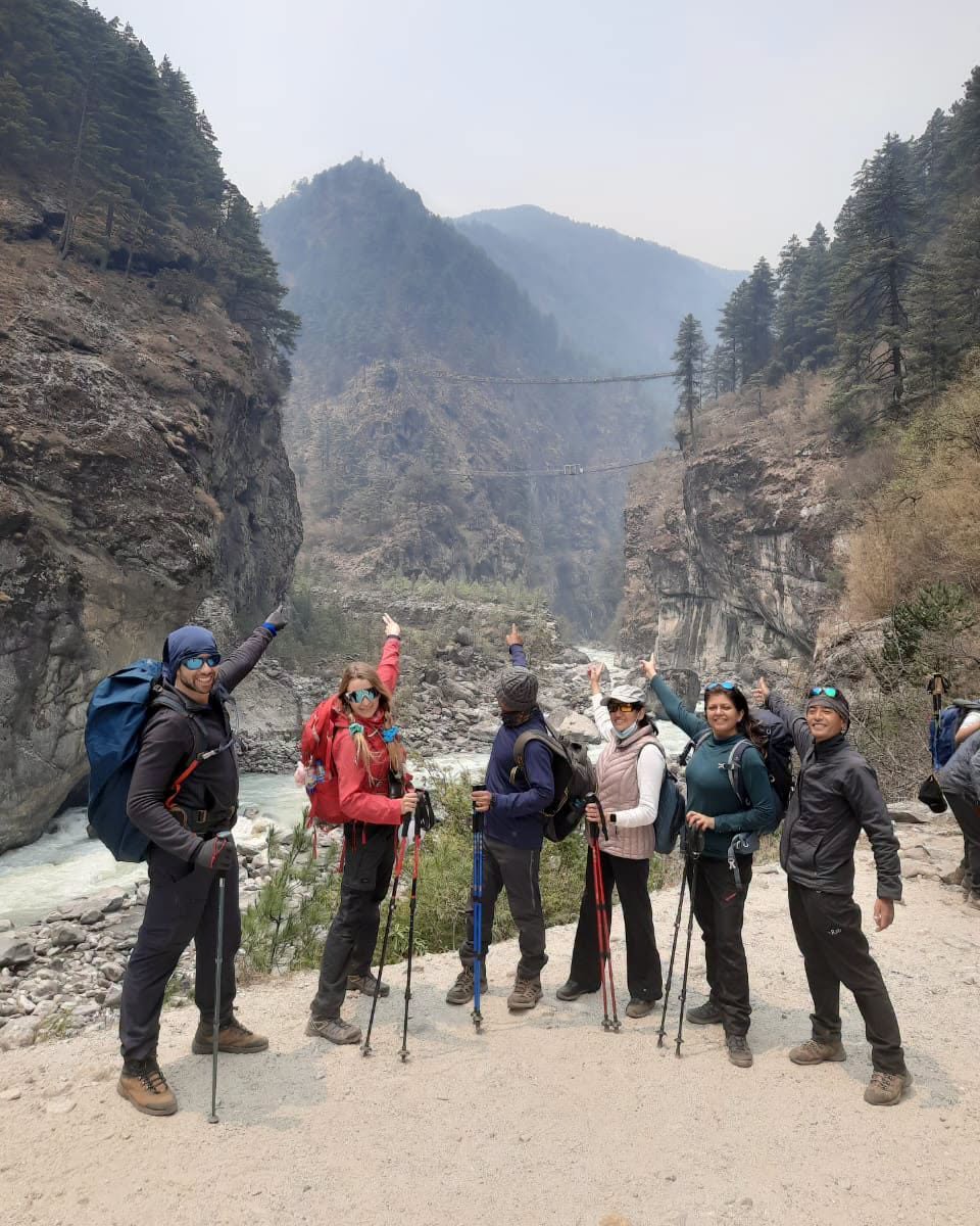 Group of hikers with trekking poles posing near a suspension bridge over a river gorge on the Everest Base Camp trail, Nepal